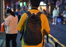A man with a backpack walks through the lively streets of Xiamen at night.